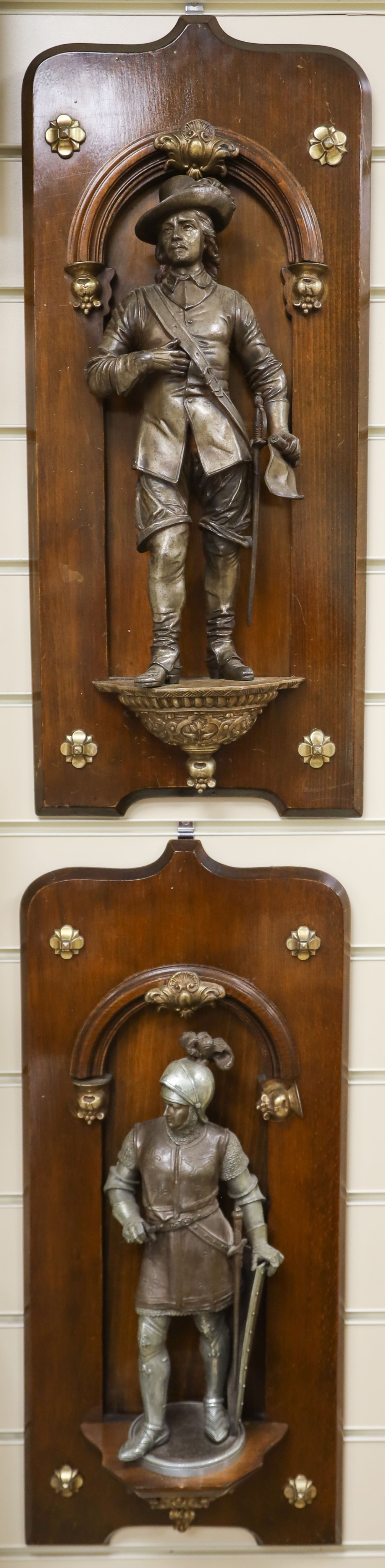 A pair of cast spelter figures of a medieval knight and a cavalier, each mounted on a mahogany niche